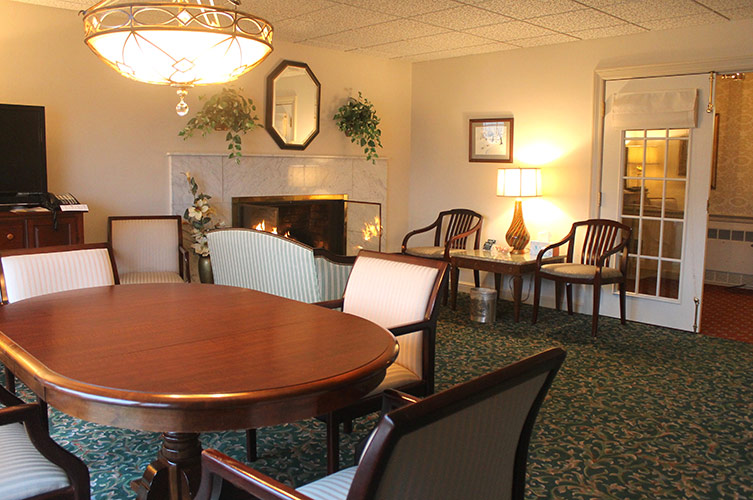 Cozy lobby lounge with round wooden table, chairs, fireplace, lamps, and carpeted seating area