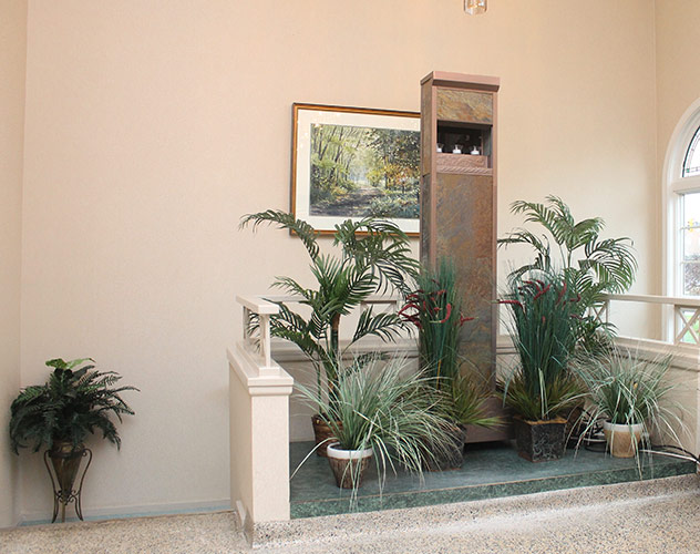 Indoor atrium with potted palm plants, a small fountain, and a framed landscape painting on beige walls