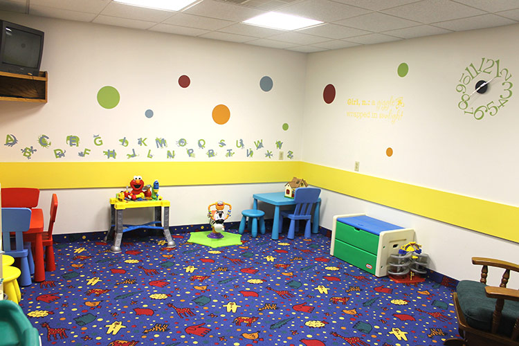 Brightly decorated daycare playroom with small tables, toys, and colorful carpet