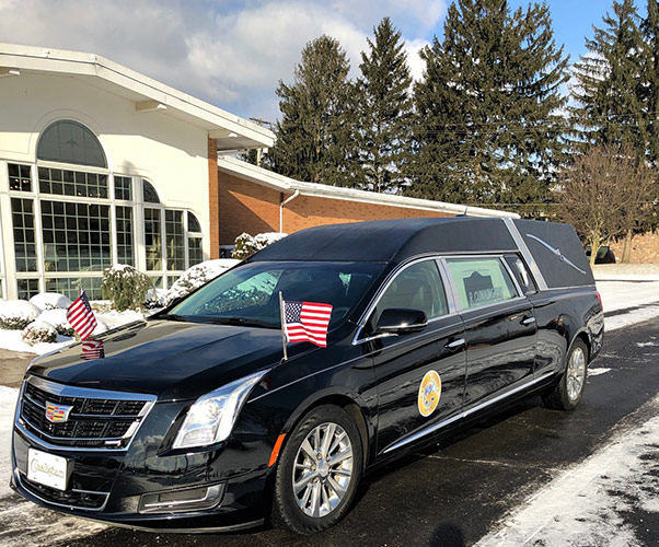 Black hearse with small American flags parked outside a building in winter.