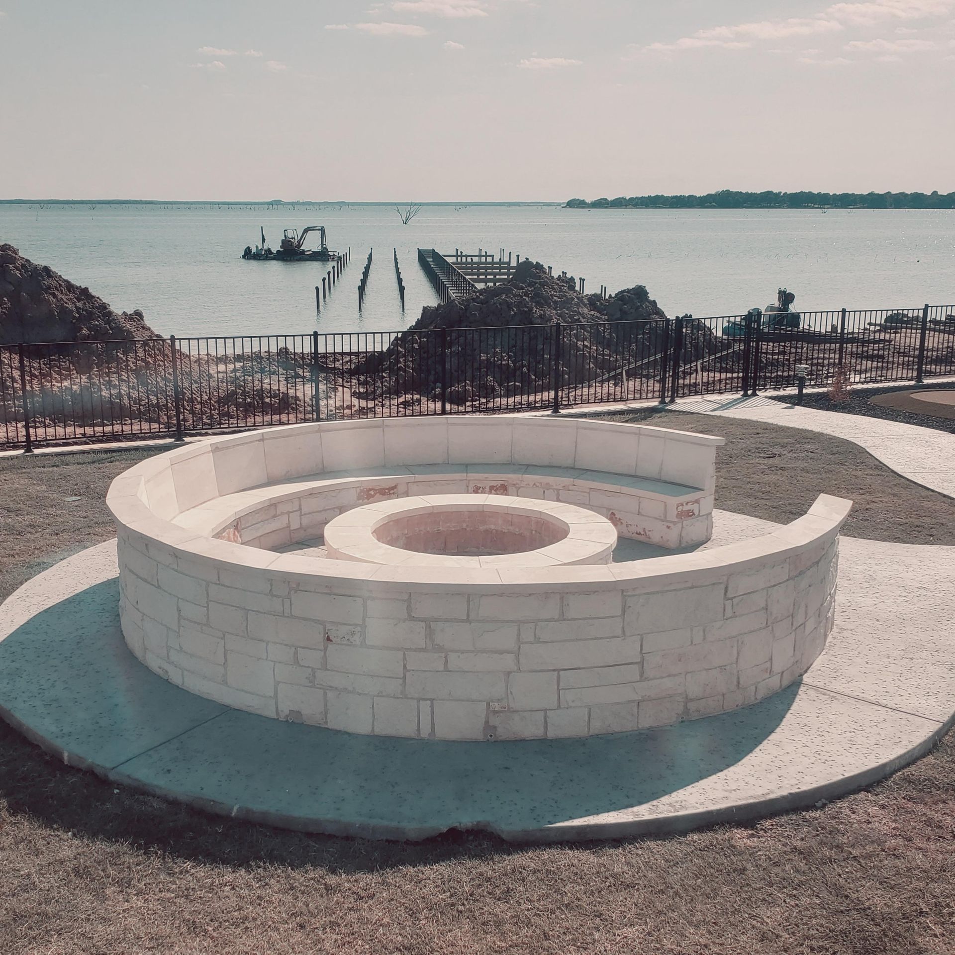 Circular white stone seating area overlooking a beach and dock on a calm waterfront