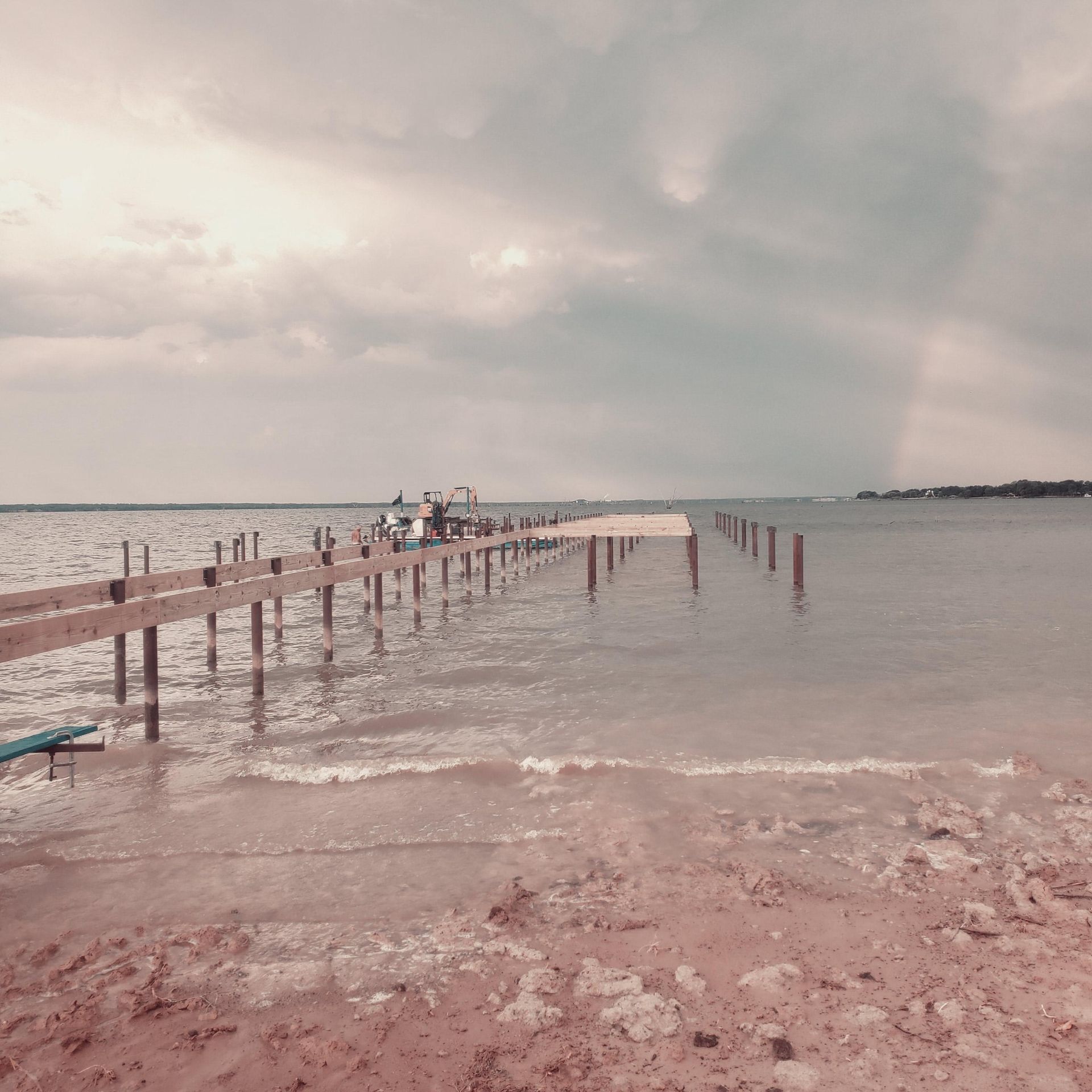 Wooden pier stretching into calm water under a cloudy sky, with people at the far end
