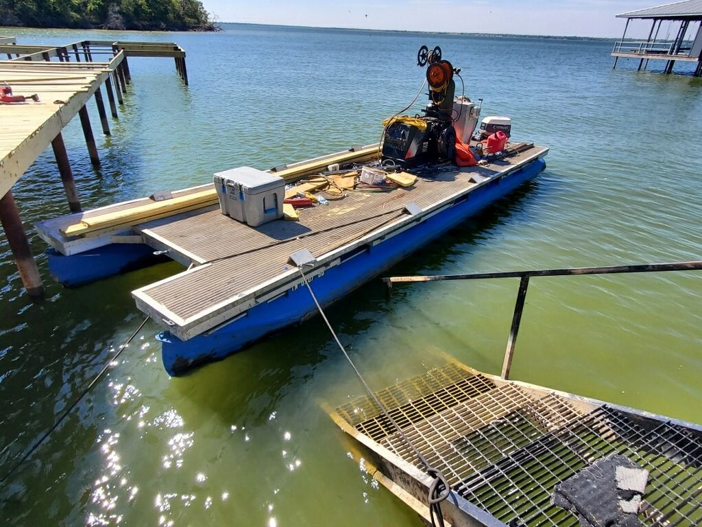 Floating workboat with crane equipment docked on calm blue water near a pier