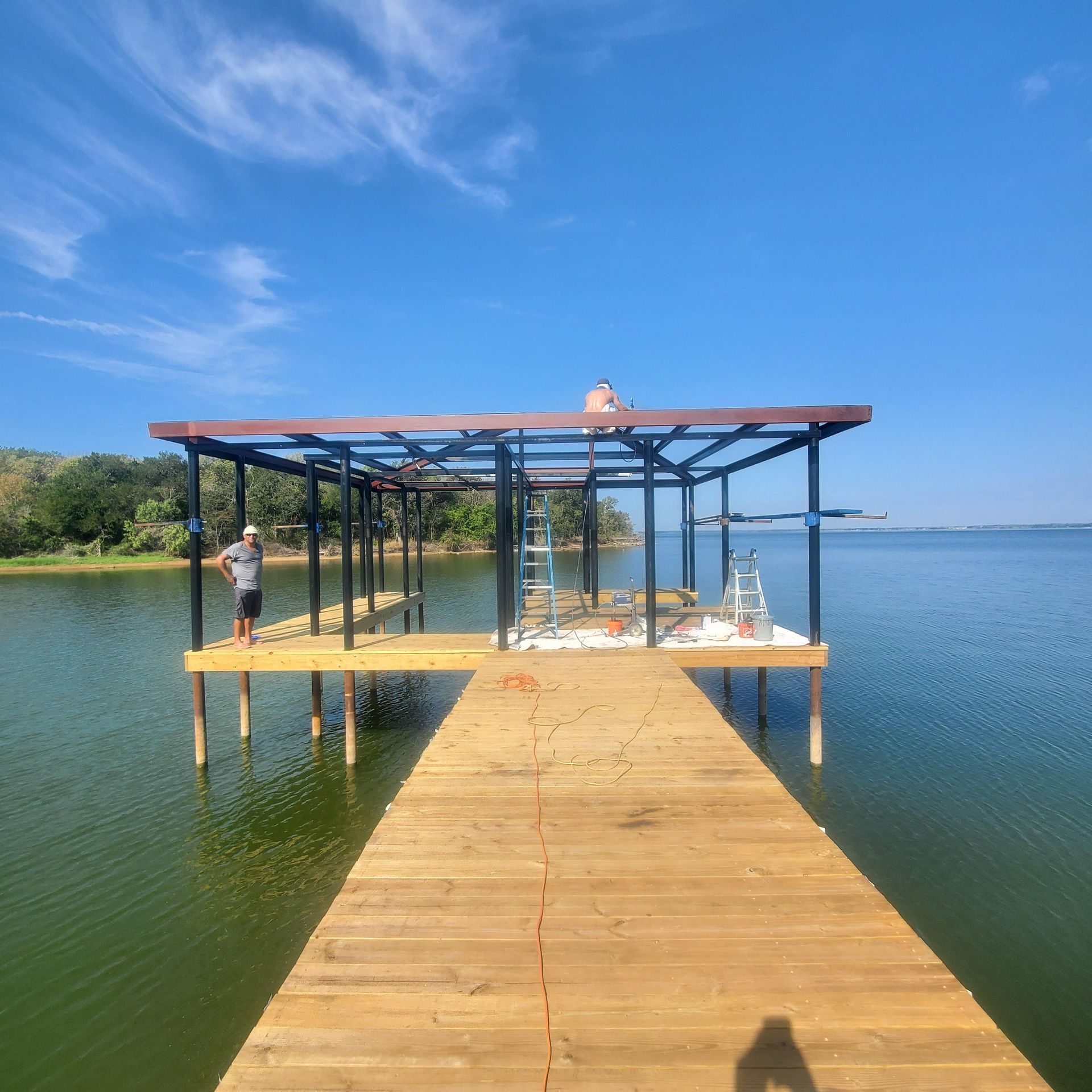 Wooden dock leading to a shaded lakeside platform over calm water under a clear blue sky.