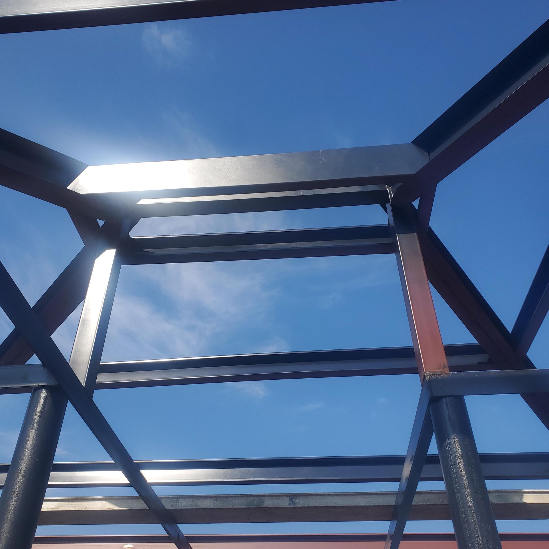 Looking up through a dark metal frame at a bright blue sky with sunlit clouds
