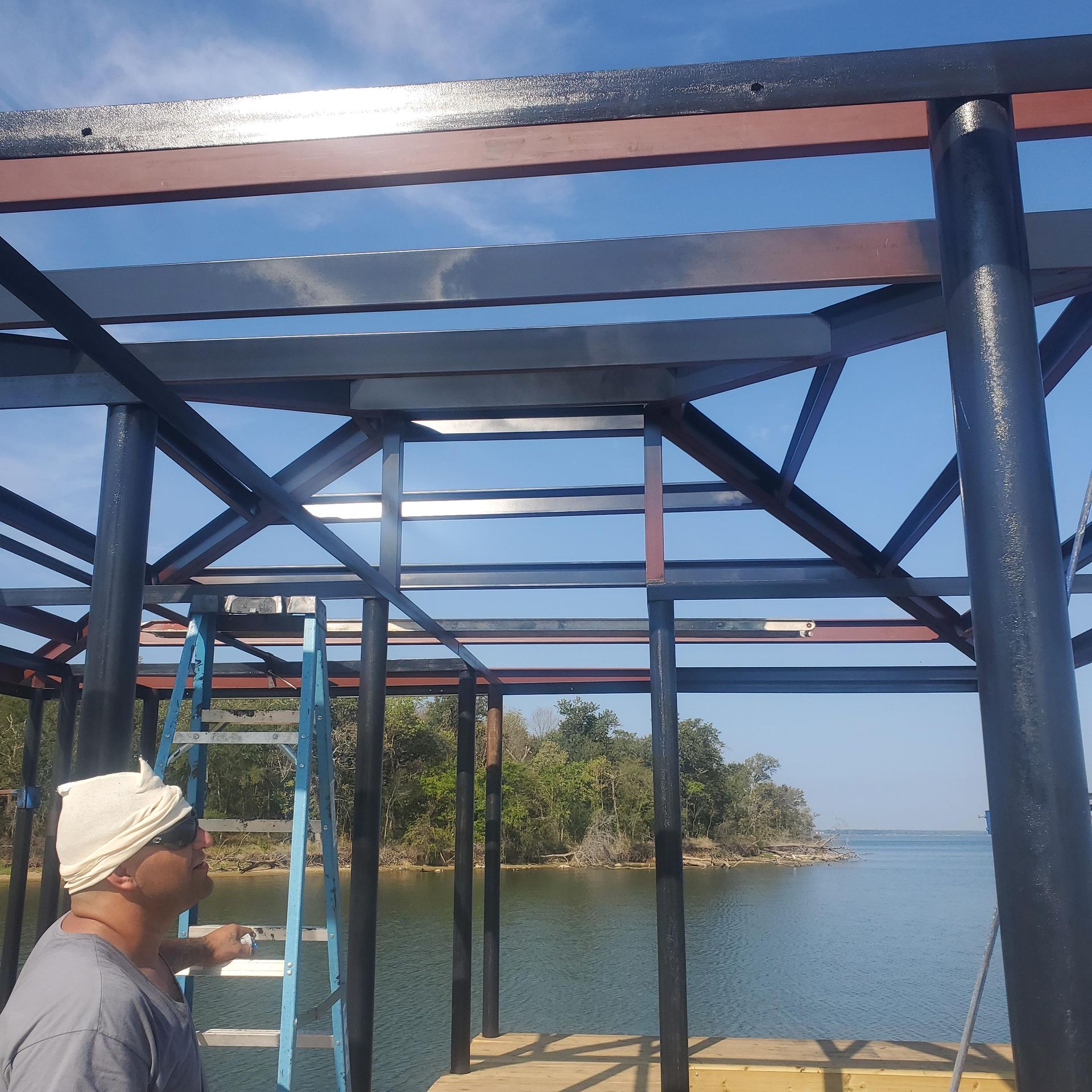 Blue metal frame overlooking a calm lake, with a person in a hat at the lower left