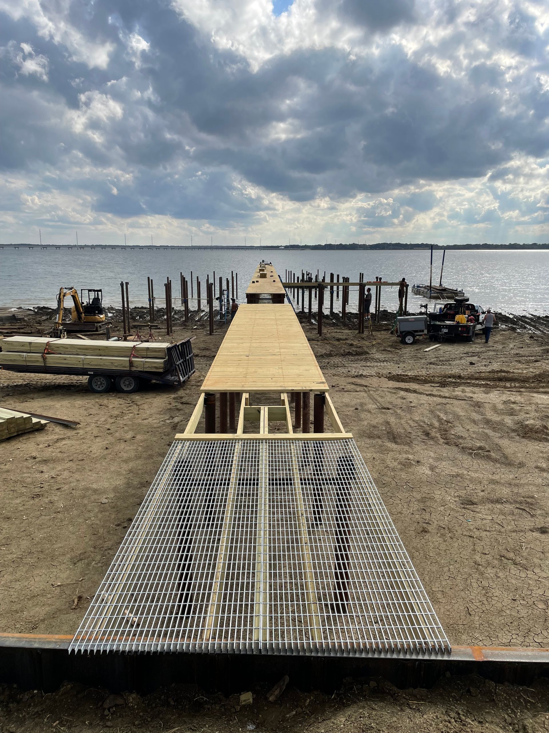 Wooden dock under construction at a muddy shoreline beneath a cloudy sky.