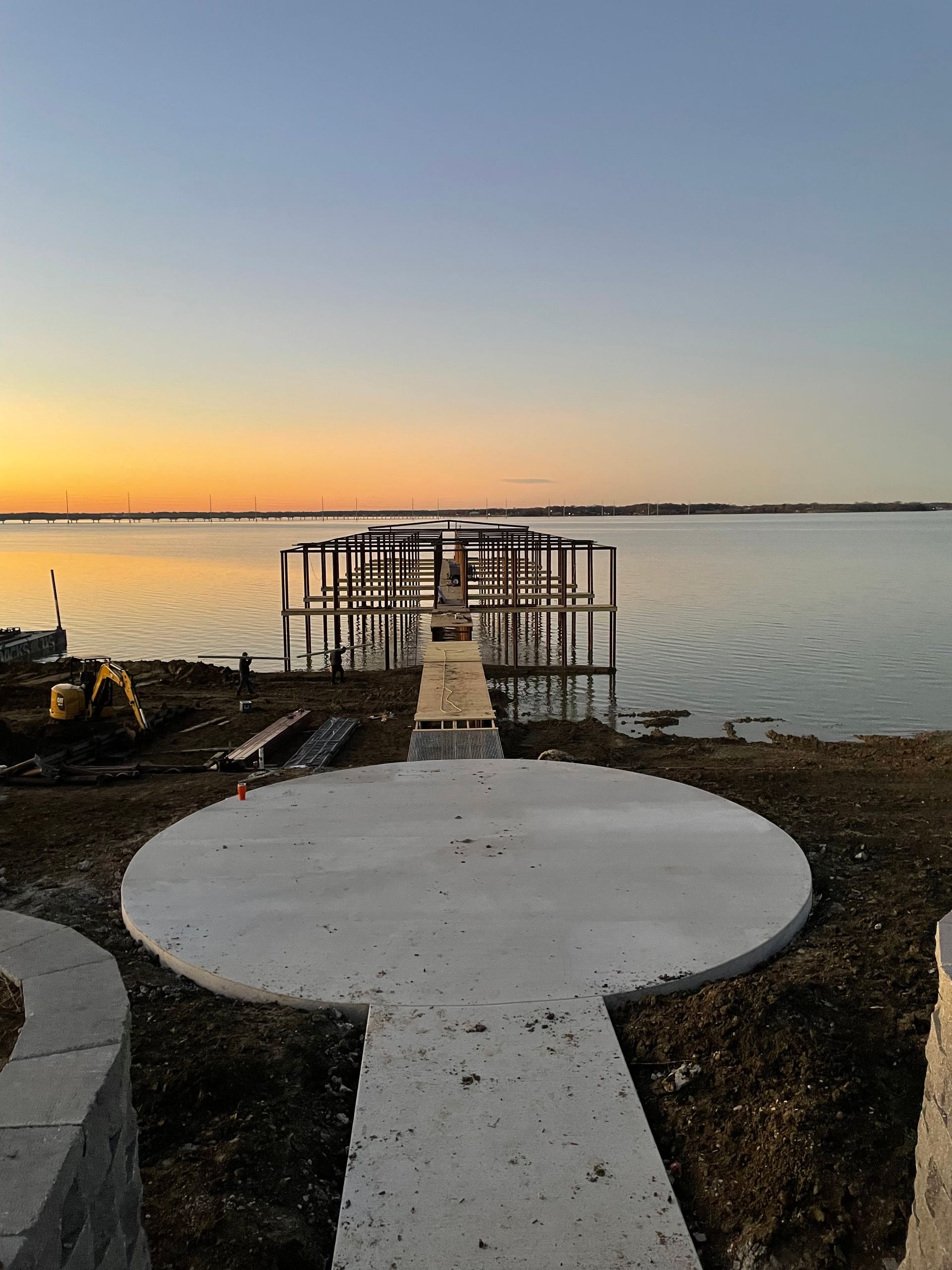 Sunset over calm water with a concrete path leading to a small dock or platform