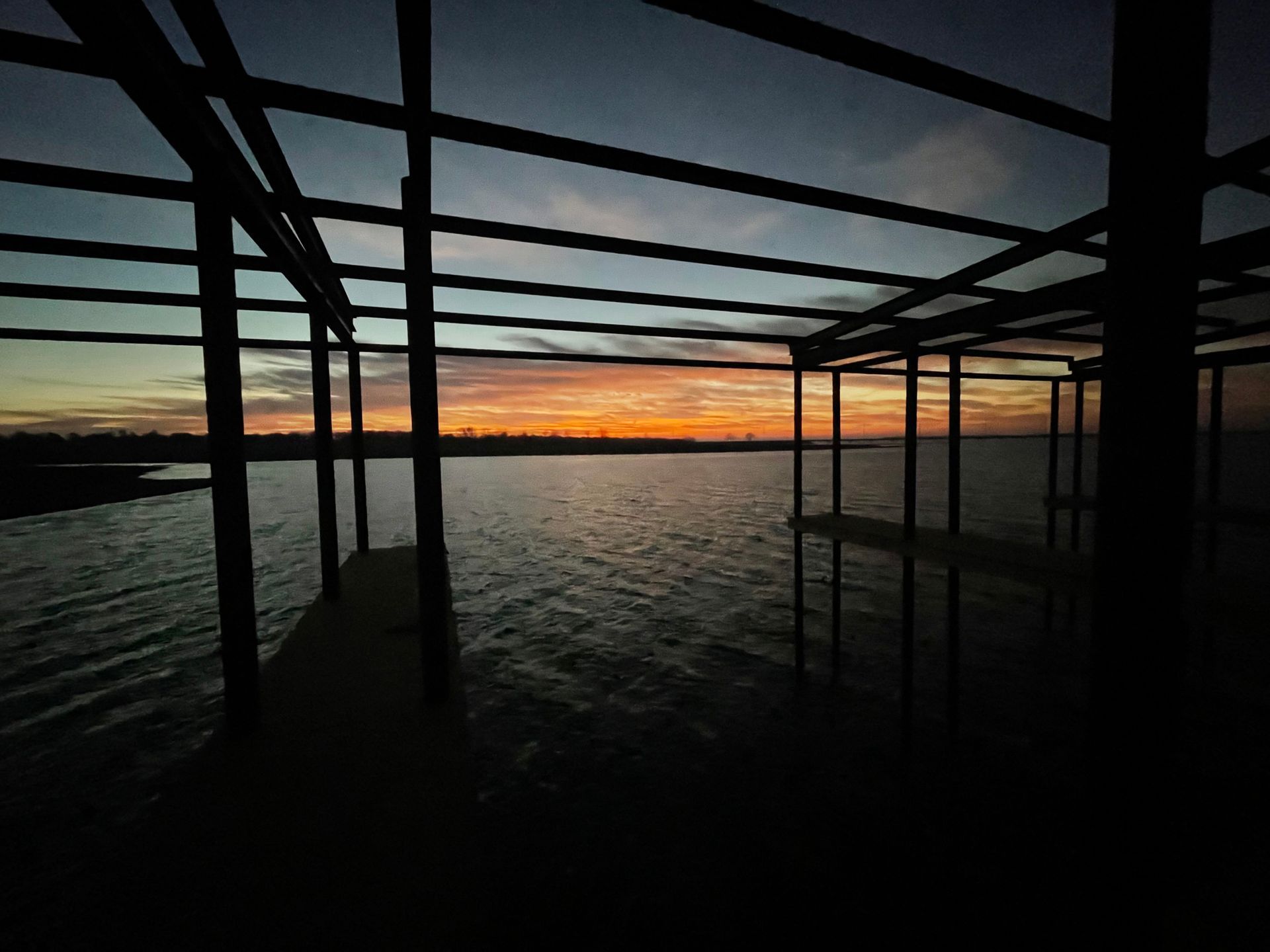 Sunset over calm water viewed from a silhouetted dock frame