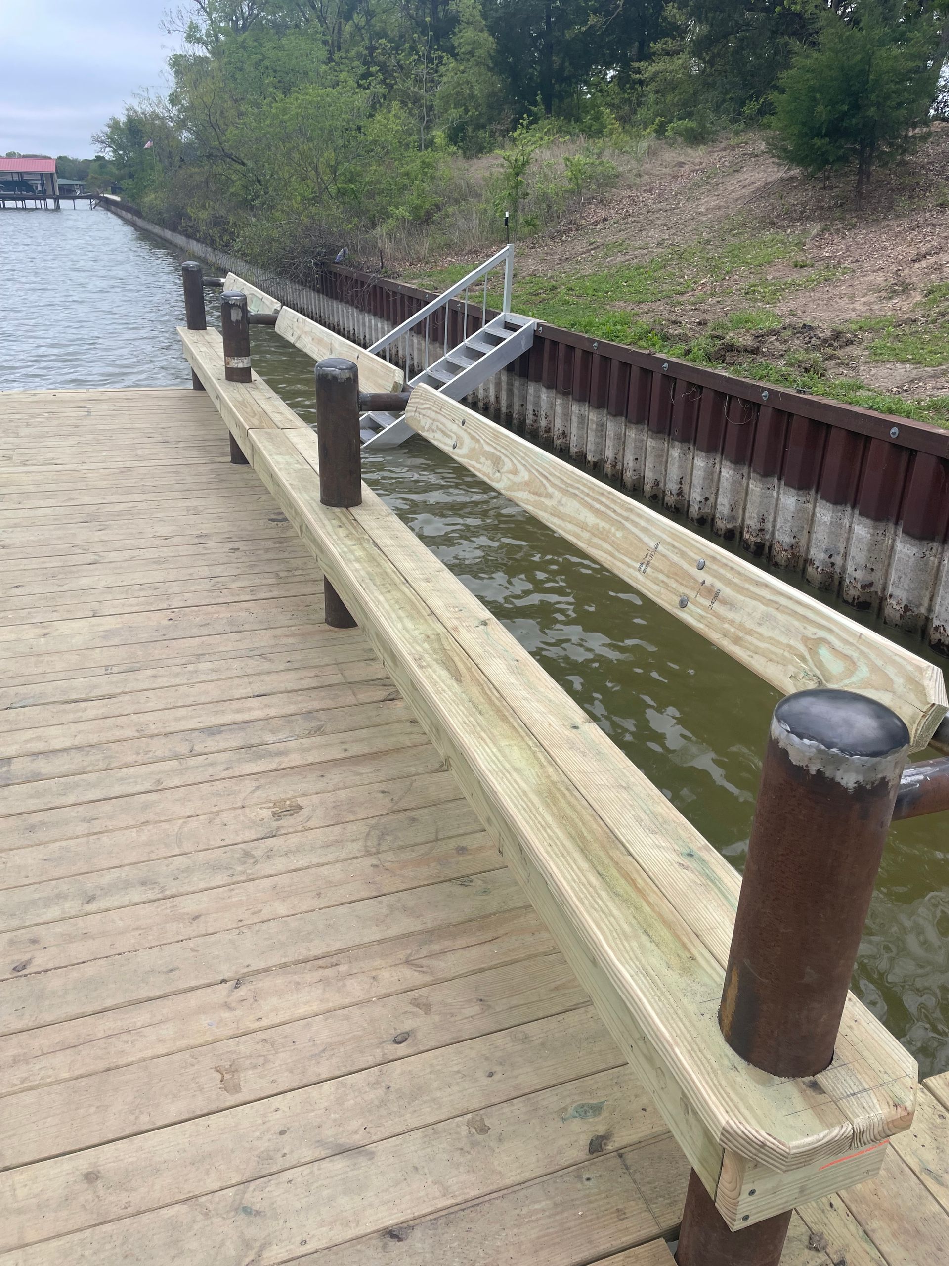 Wooden boardwalk beside a narrow canal with metal ladder and grassy embankment