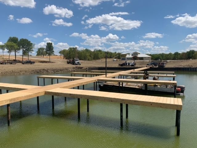 New wooden dock under construction on a calm lake, with workers and trucks onshore under a blue sky