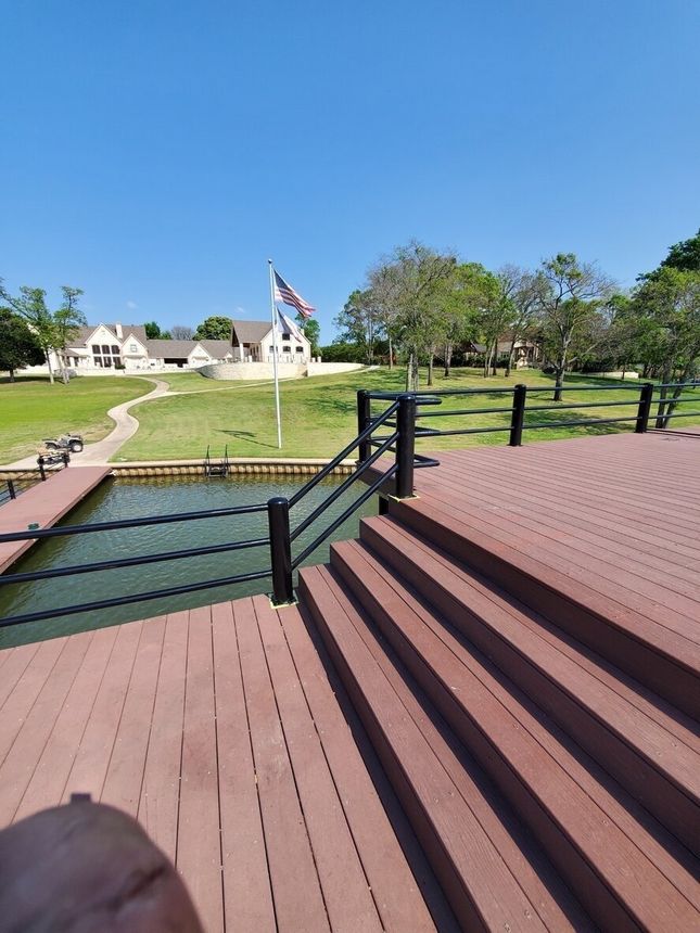 Wooden steps by a canal leading to a grassy park with a house and American flag under a clear blue sky