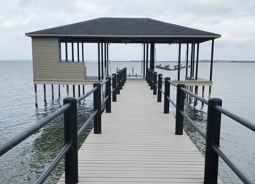 Wooden pier with railings leading to a small covered dock over calm water
