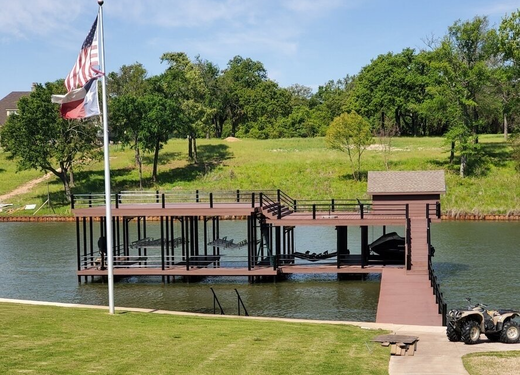 Wooden dock on a lake with an American flag, trees, and grassy park shoreline