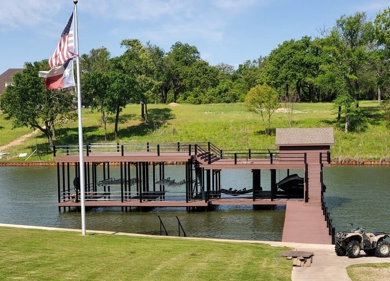 Dock with American flag by a calm lake, green hillside, and trees under a blue sky