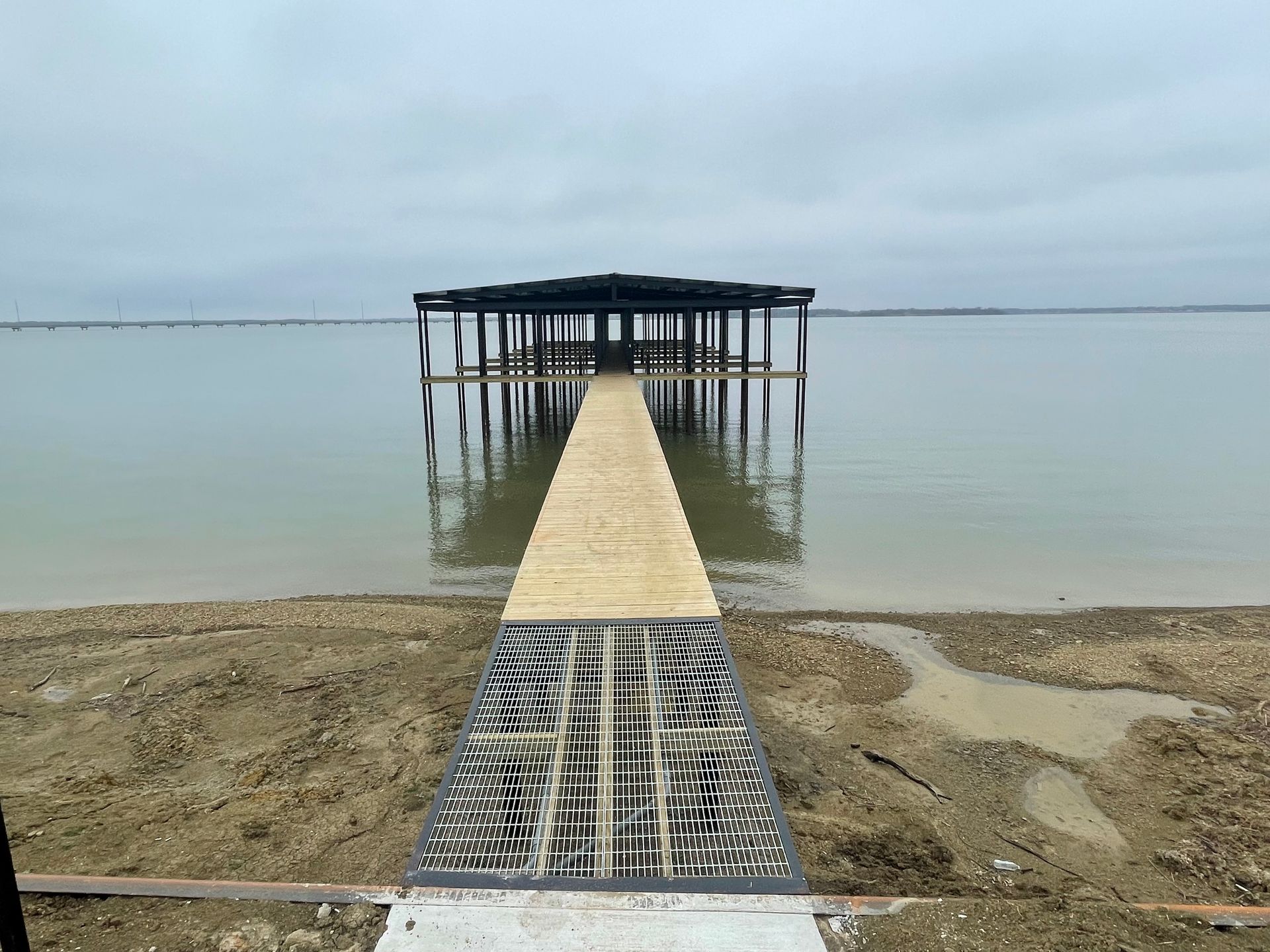 Wooden pier leading to a small dock over calm water on a cloudy beach.