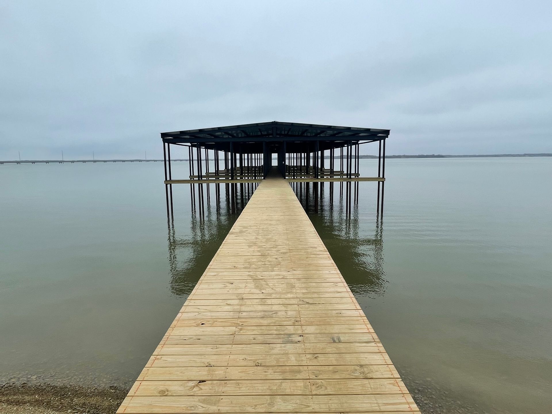 Wooden pier leading to a small roofed platform over calm water under a cloudy sky