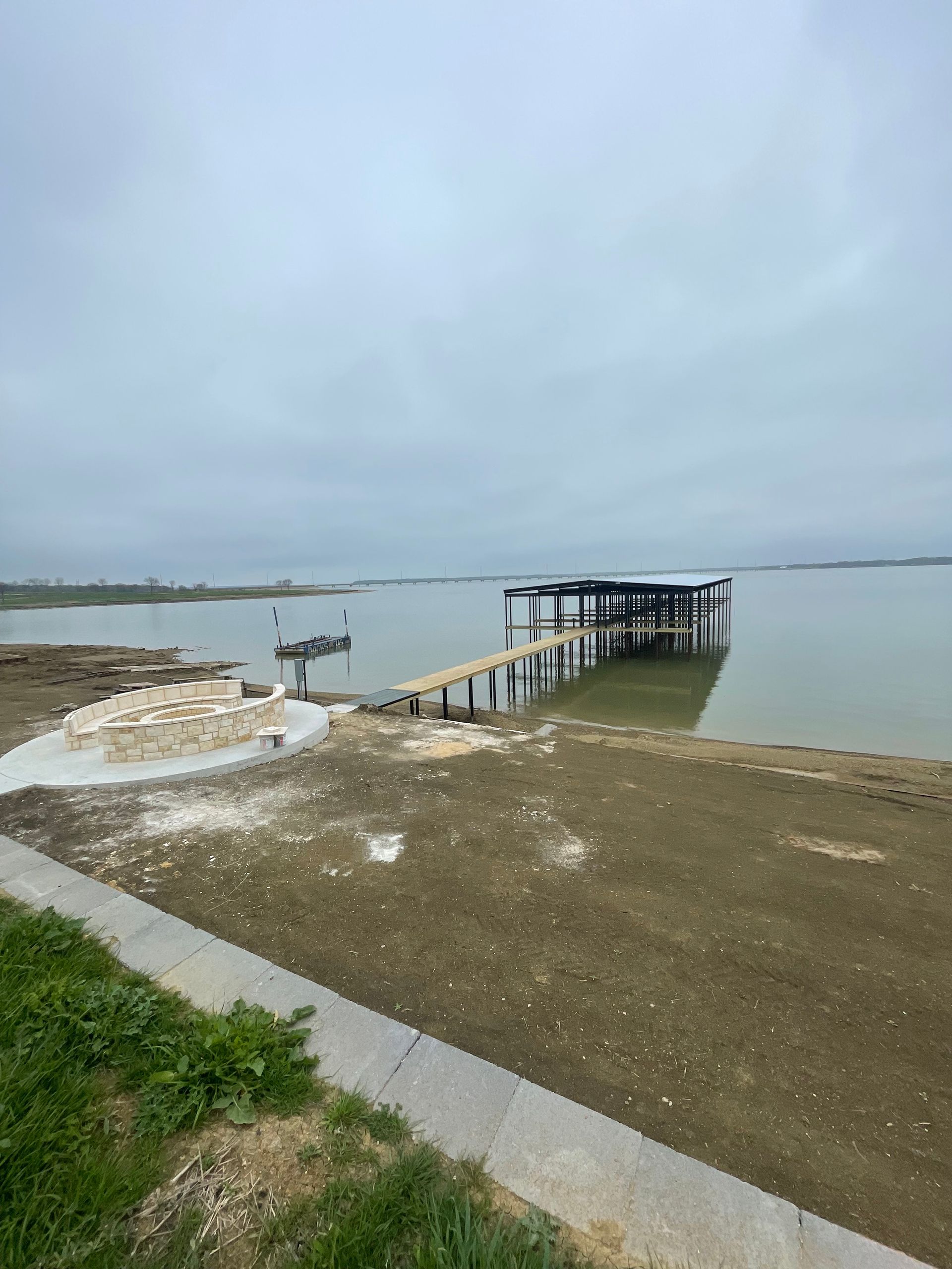 Shoreline with a wooden dock extending into a calm lake under a cloudy sky