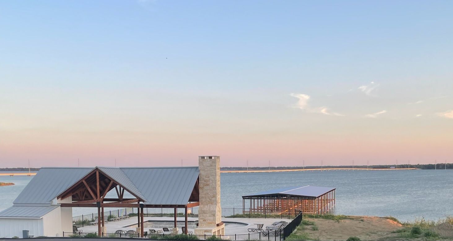 Calm seaside at sunset with small waterfront shelters and a dock under a pastel sky