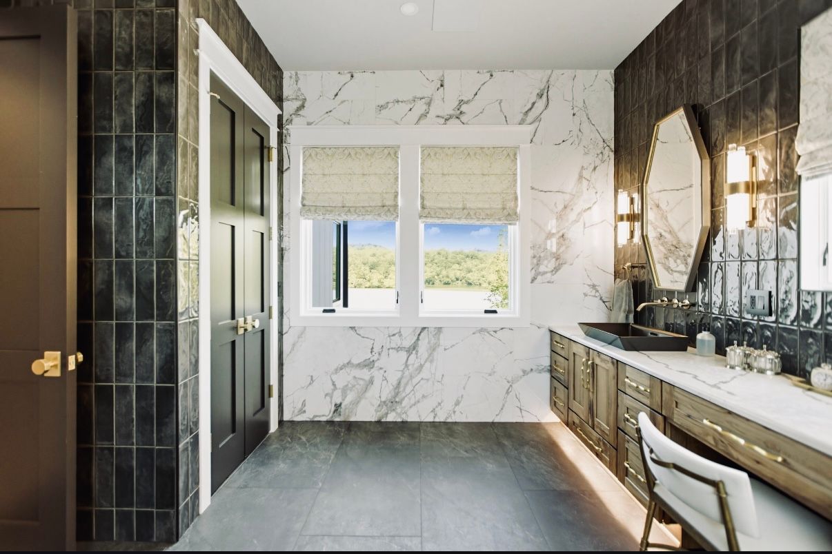 Bathroom vanity under arched herringbone tile wall with mirror; navy cabinets and marble countertop.