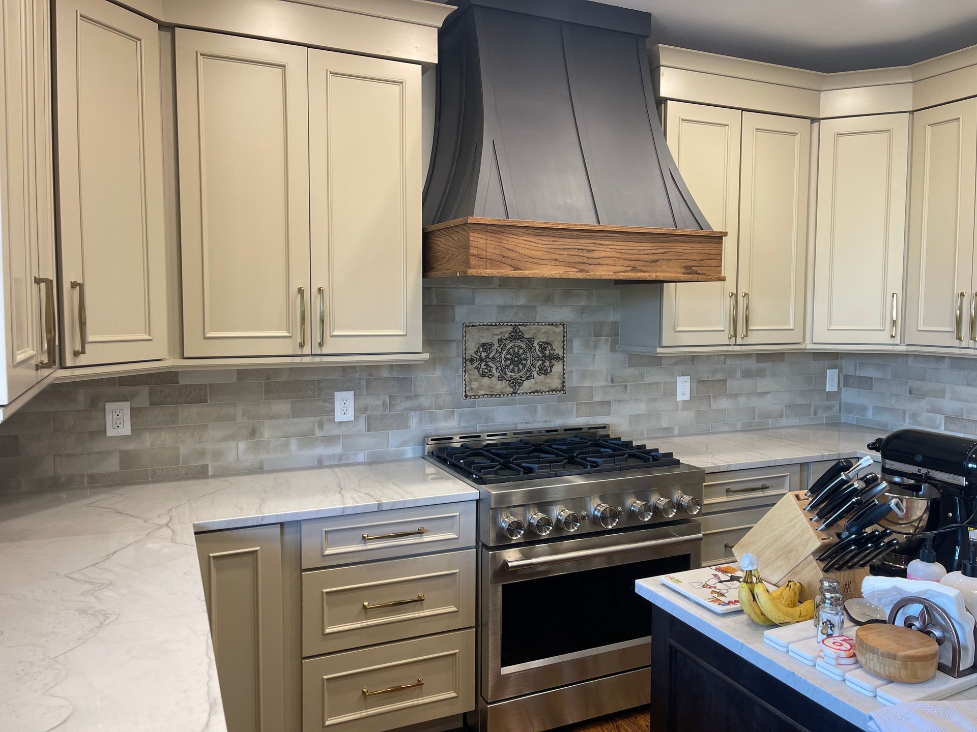 Modern kitchen with marble backsplash, white cabinets, open shelves, and gold fixtures around a central sink.