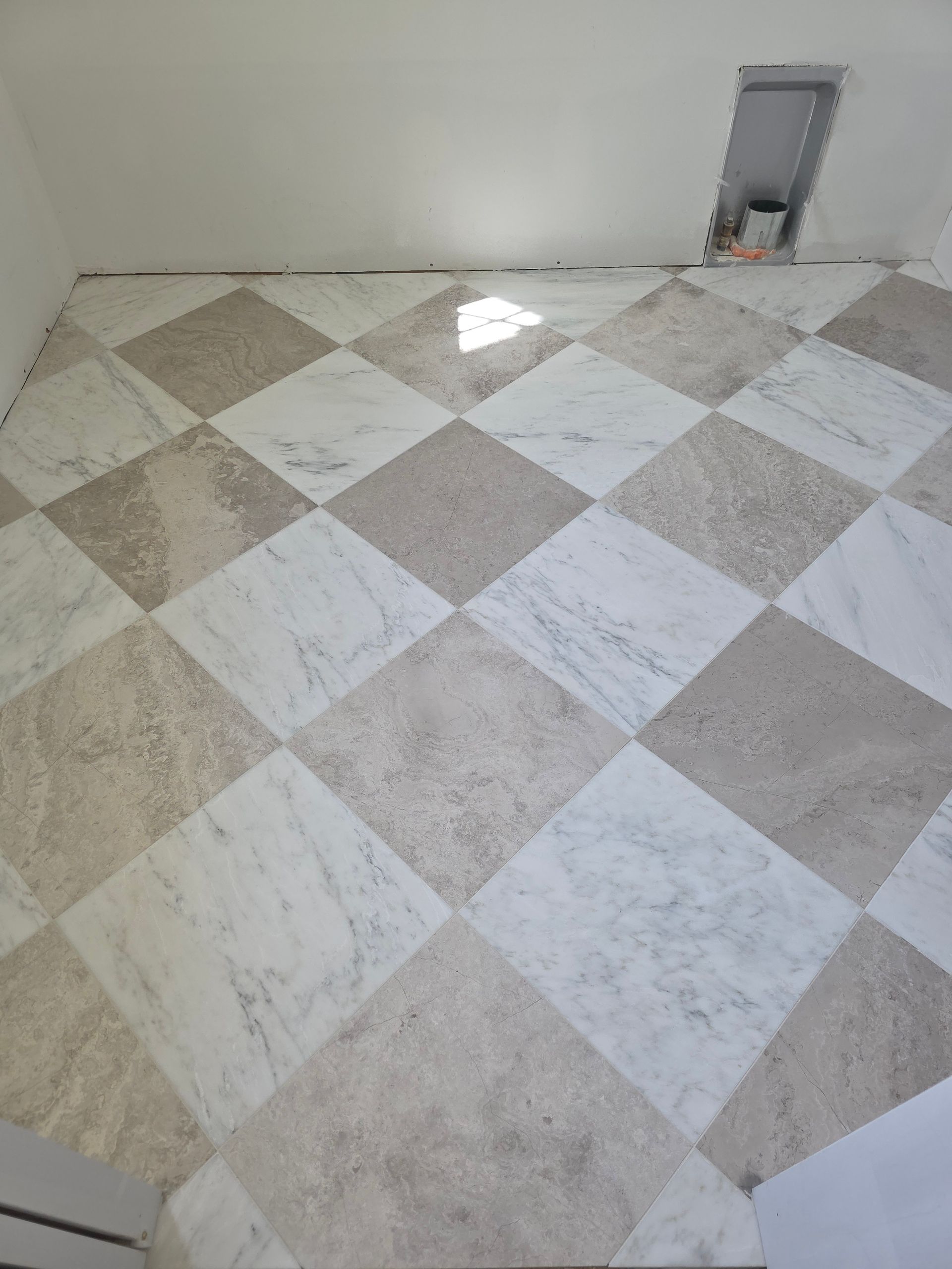 Person laying gray floor tile over adhesive with spacers and trowel on a subfloor