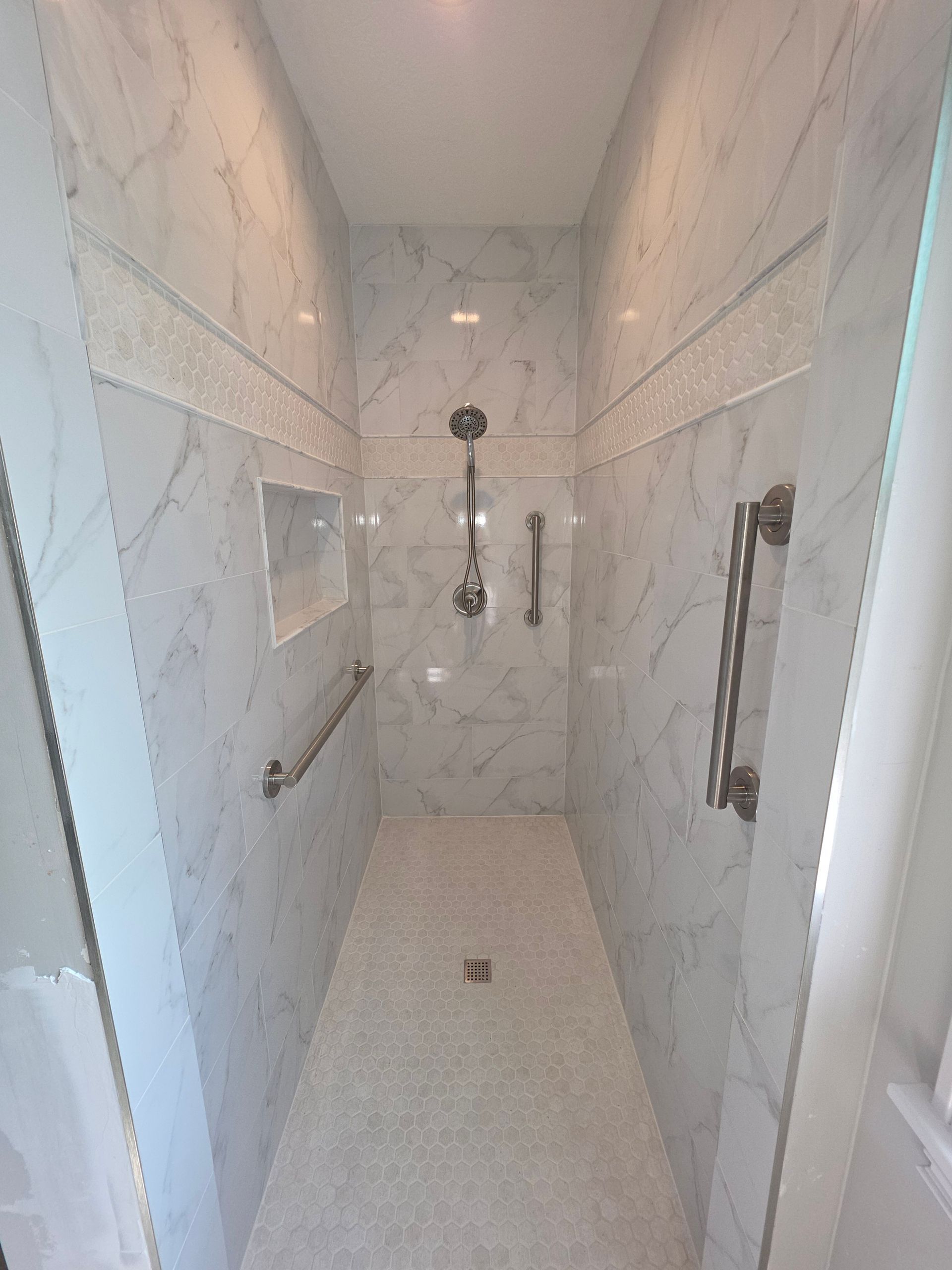 Small beige hotel shower stall with handheld showerhead, grab bars, and a curtain on the left