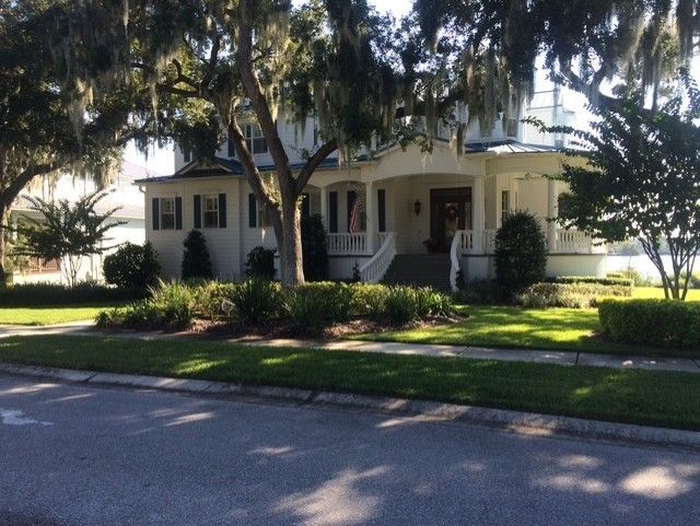 Suburban house with front porch, large trees, and a sunlit lawn beside a quiet street Suburban house with front porch, large trees, and a sunlit lawn beside a quiet street