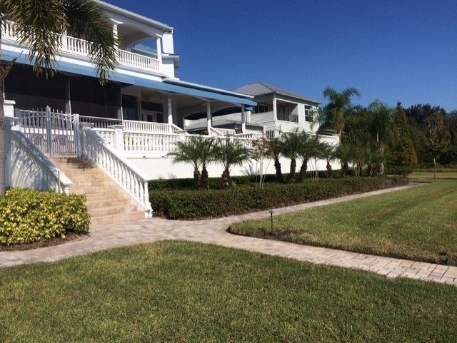 Large white house with a blue roof, front stairs, porch, and landscaped lawn under a clear sky