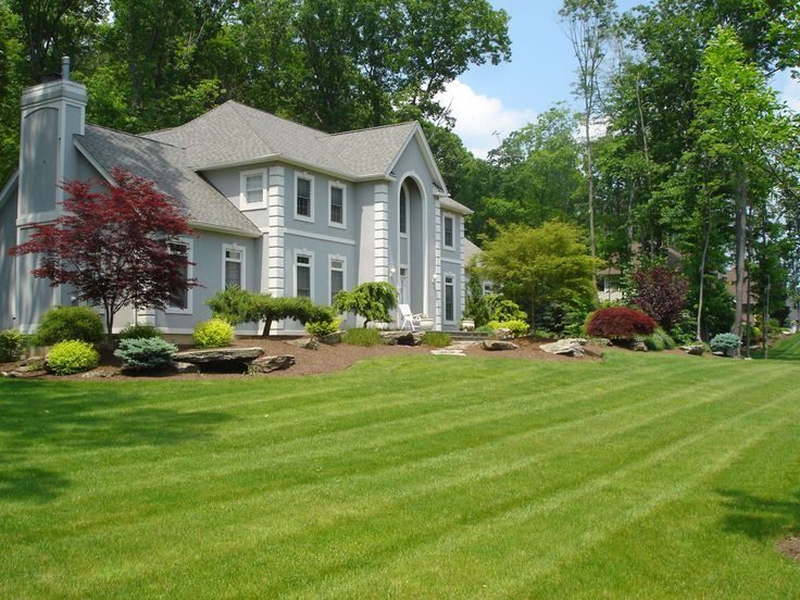 Large gray house with white trim and a manicured green lawn, surrounded by trees and shrubs