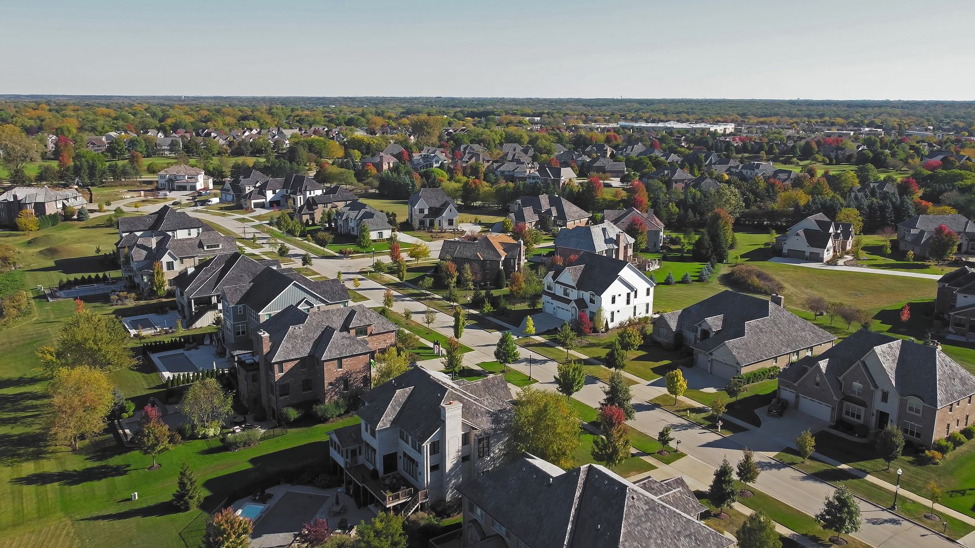 Aerial view of a suburban neighborhood with houses, streets, trees, and a distant skyline. Aerial view of a suburban neighborhood with houses, streets, trees, and a distant skyline.
