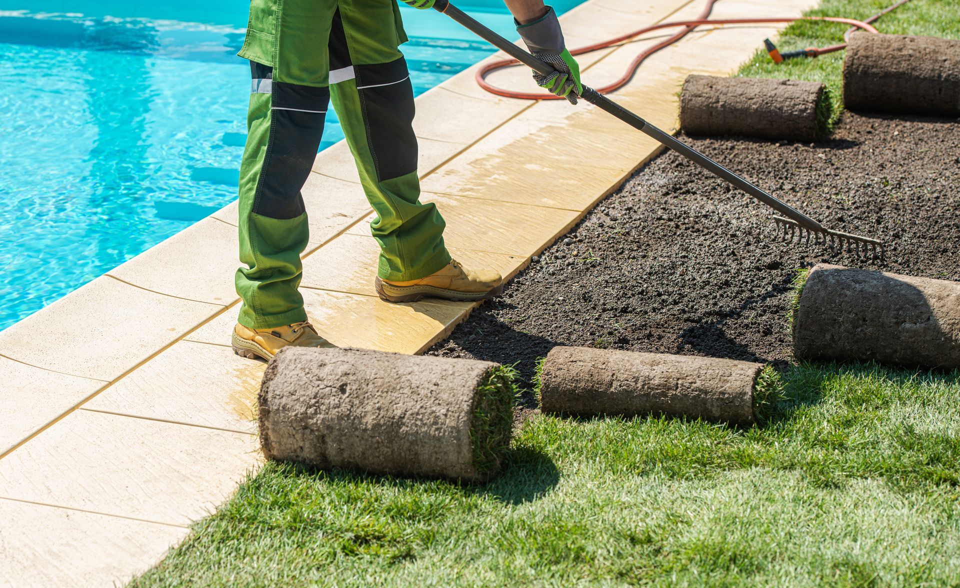 Worker rolling sod beside a pool, laying new grass along the concrete edge.