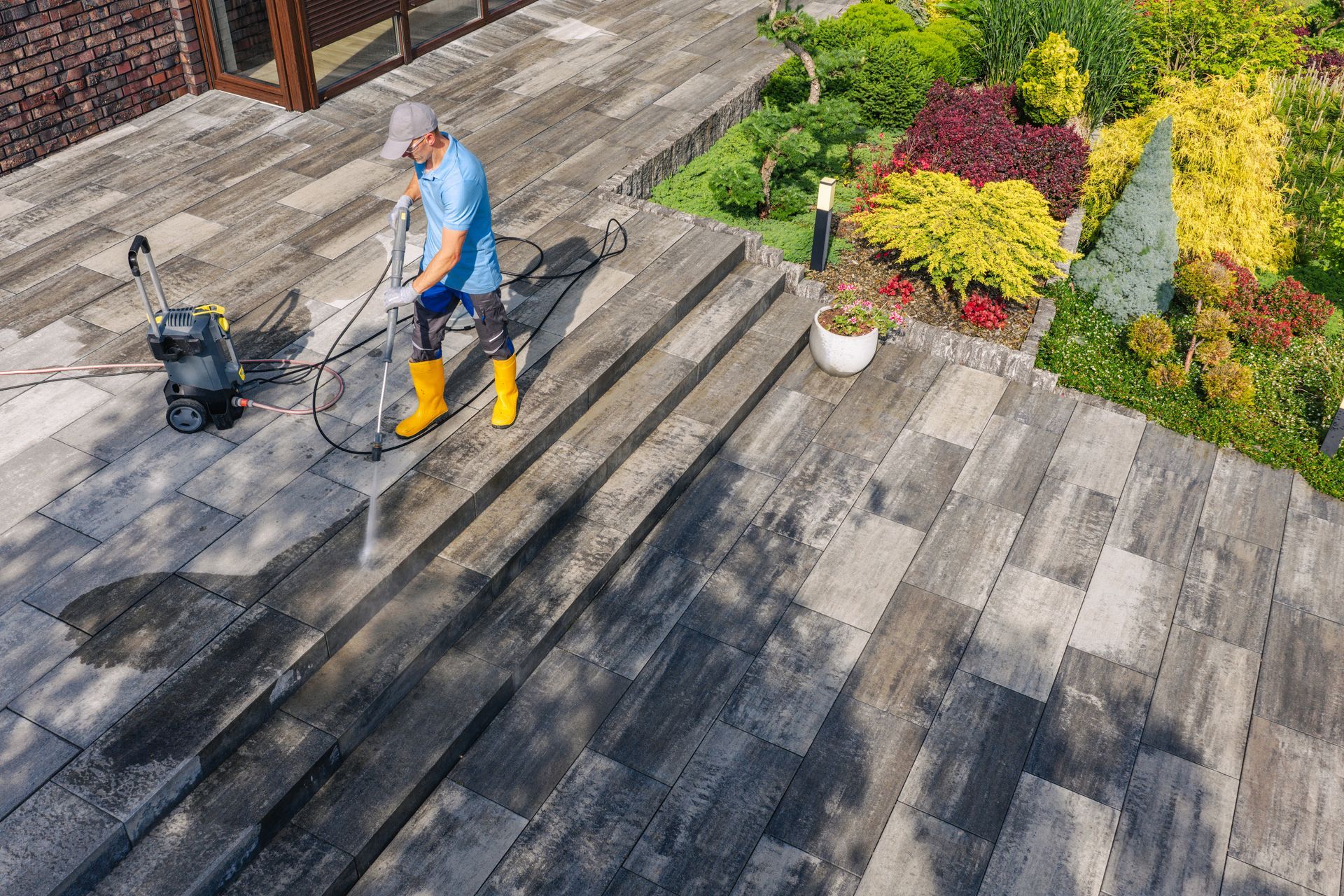 Worker power-washing a weathered wooden deck beside a garden. Worker power-washing a weathered wooden deck beside a garden.