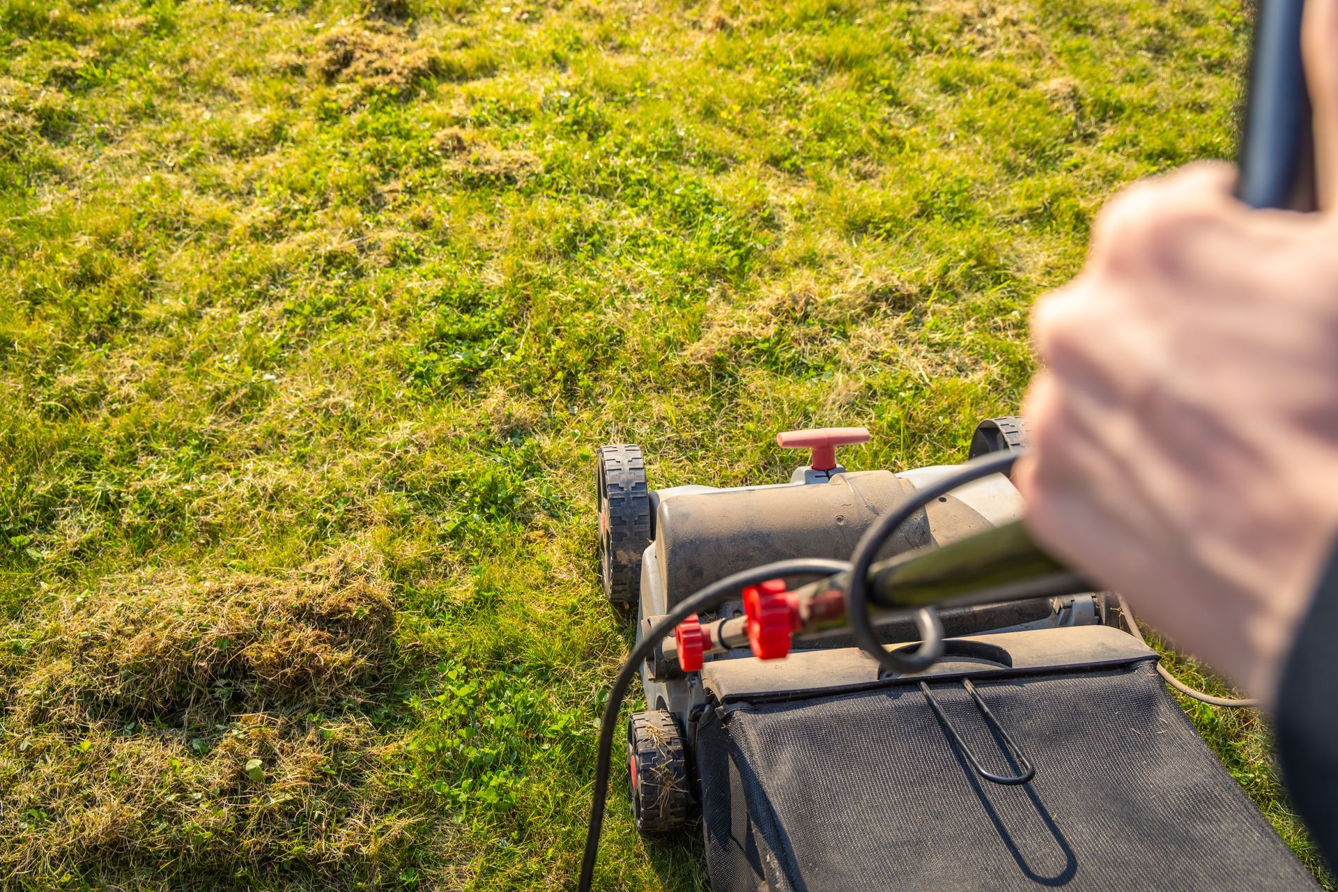 Hands operating a lawn mower on green grass outdoors Hands operating a lawn mower on green grass outdoors