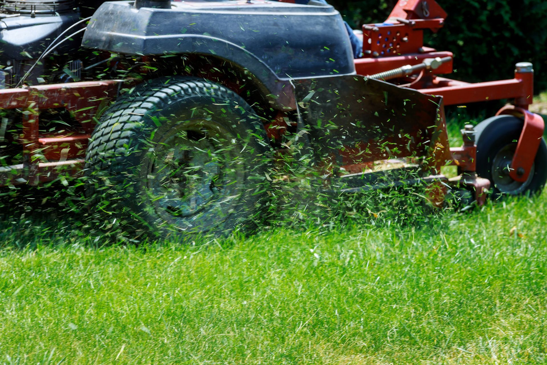 Red lawn mower cutting green grass, with clippings flying across the yard. Red lawn mower cutting green grass, with clippings flying across the yard.