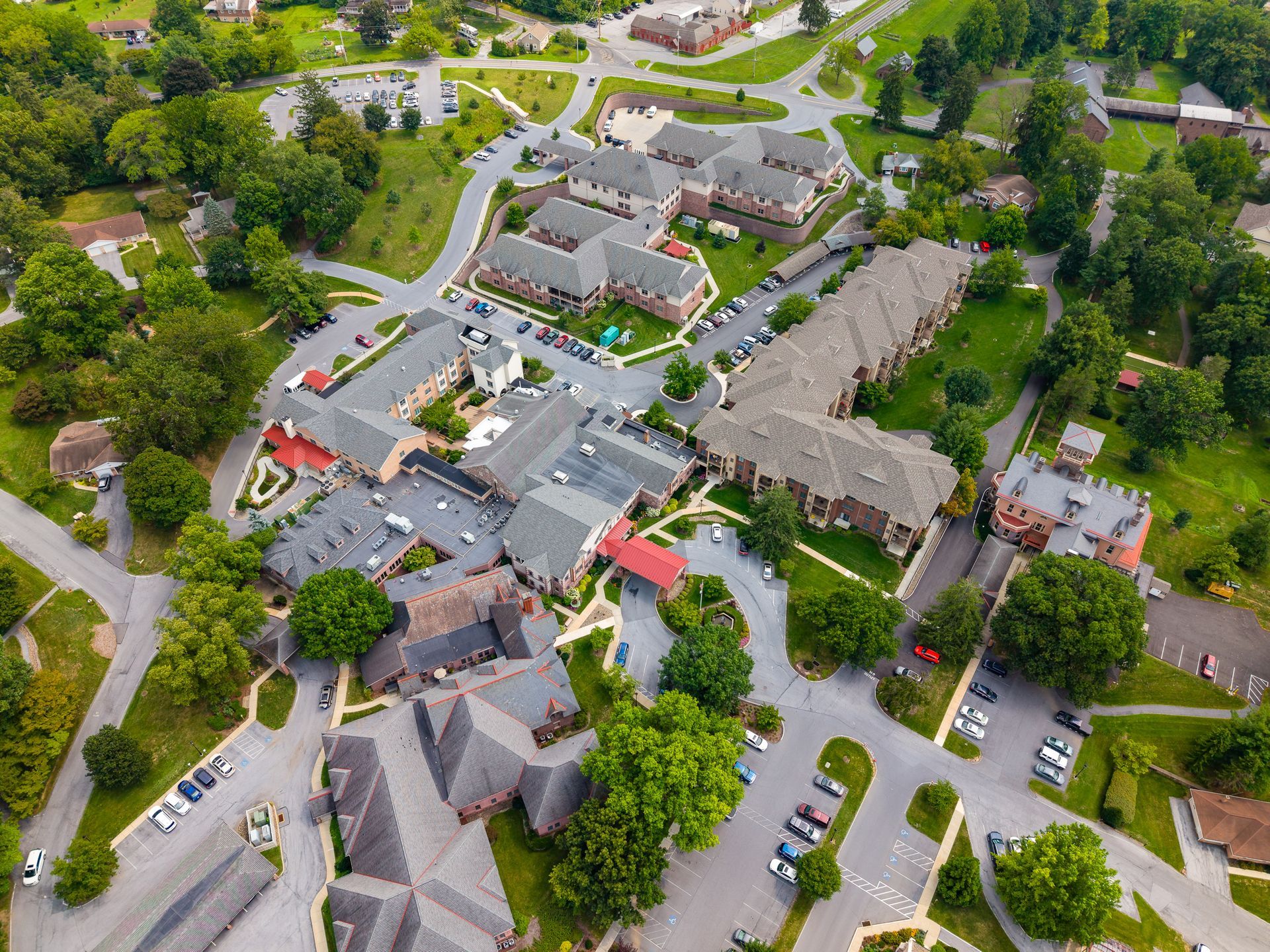 Aerial view of a campus with several gray-roofed buildings, trees, roads, and parked cars. Aerial view of a campus with several gray-roofed buildings, trees, roads, and parked cars.