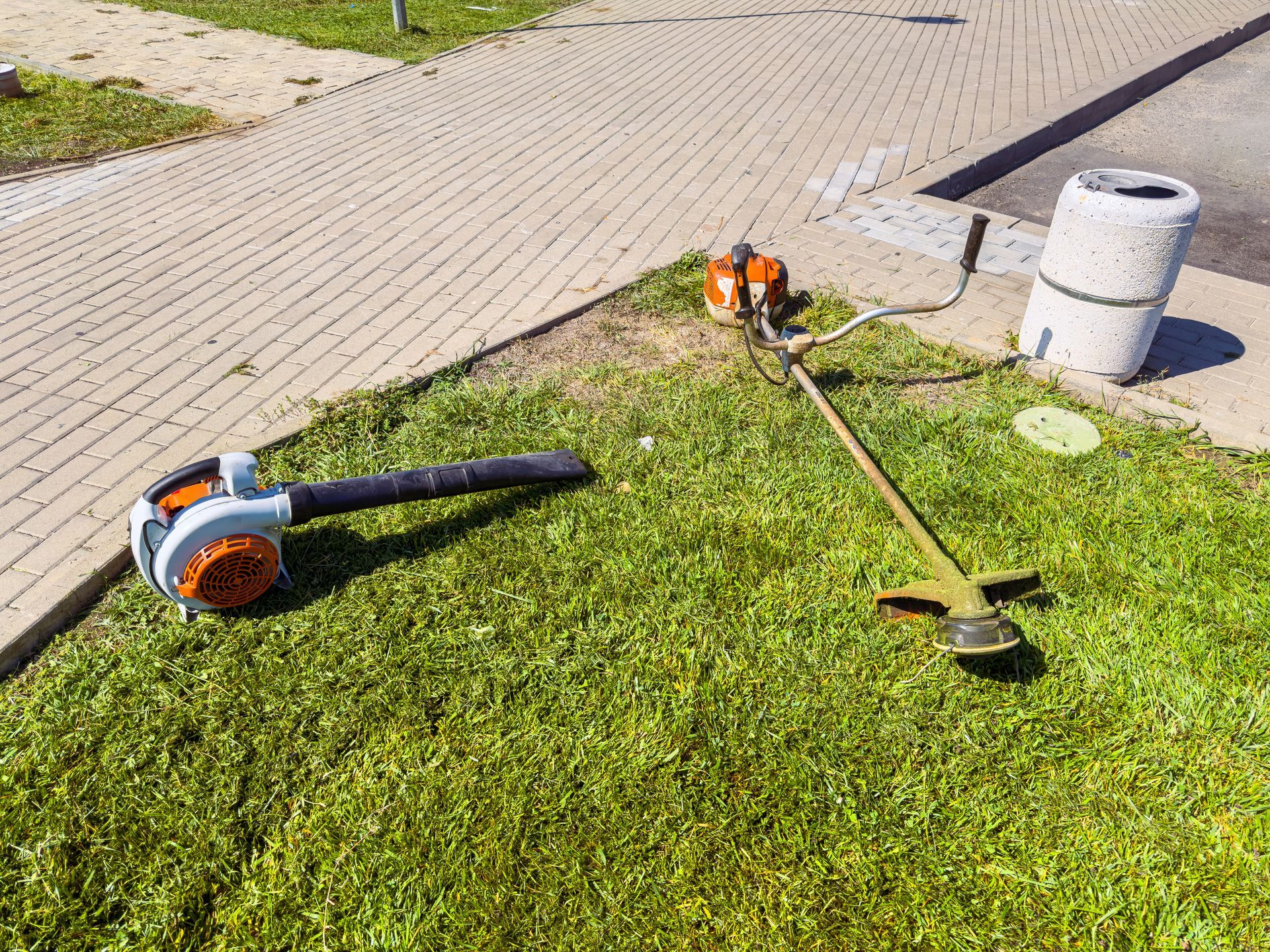 Two garden tools on grass beside a paved path and a concrete post Two garden tools on grass beside a paved path and a concrete post