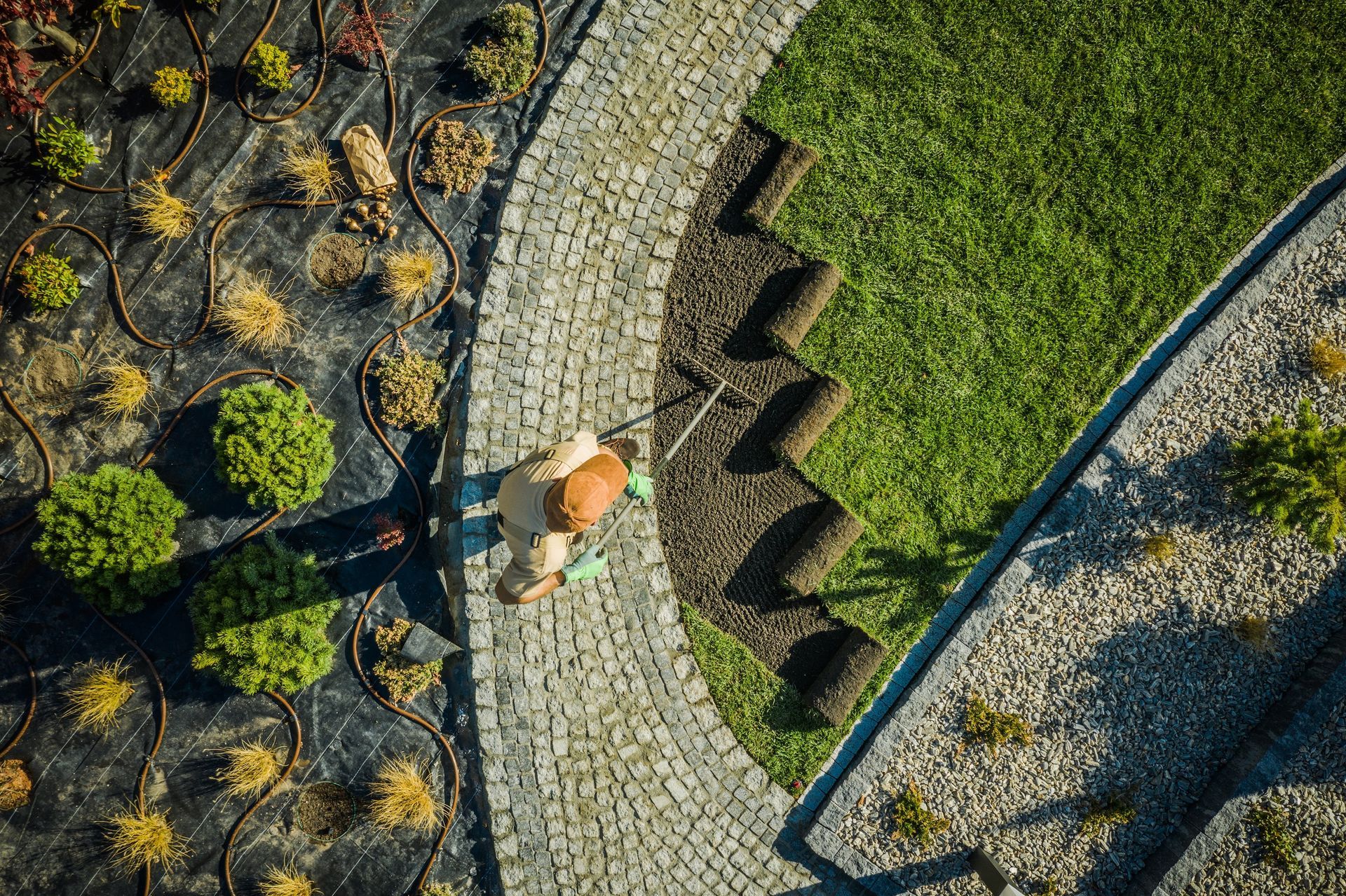Overhead view of a person in an orange hat walking along a curved stone path beside green and rocky landscaping Overhead view of a person in an orange hat walking along a curved stone path beside green and rocky landscaping
