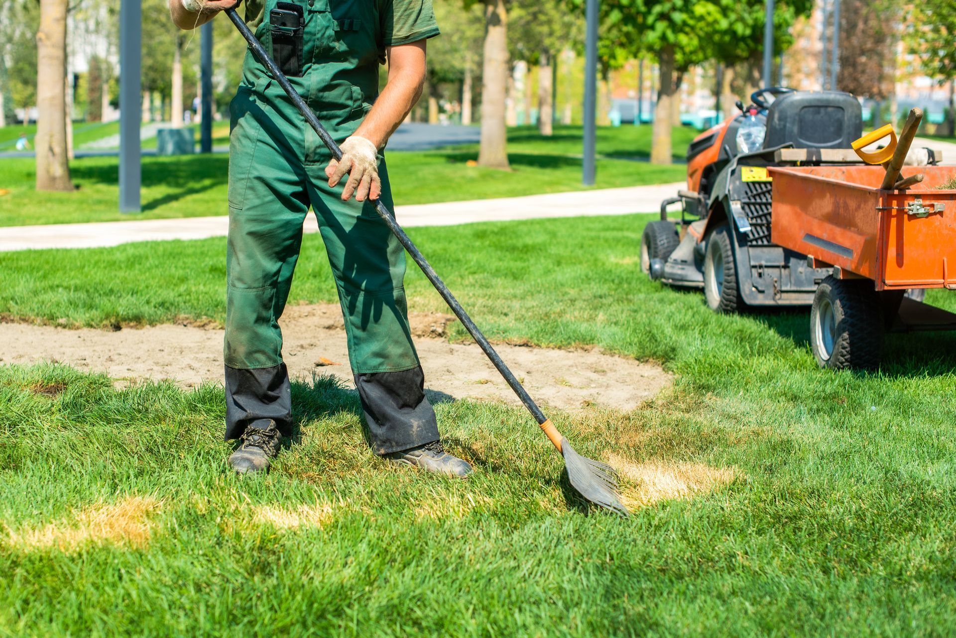 Worker mowing grass beside a landscaping cart in a sunny park Worker mowing grass beside a landscaping cart in a sunny park
