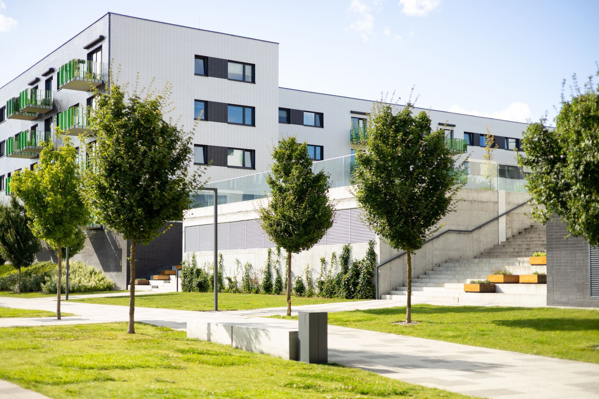 Modern white apartment building with trees, lawns, and a sloped walkway under a bright sky Modern white apartment building with trees, lawns, and a sloped walkway under a bright sky