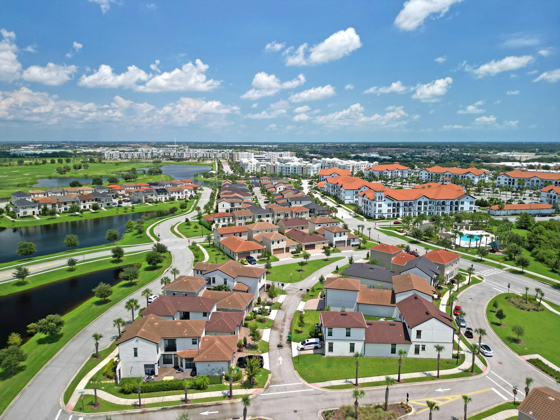 Aerial view of a suburban neighborhood with red-roofed houses, winding roads, and a pond under a blue sky. Aerial view of a suburban neighborhood with red-roofed houses, winding roads, and a pond under a blue sky.