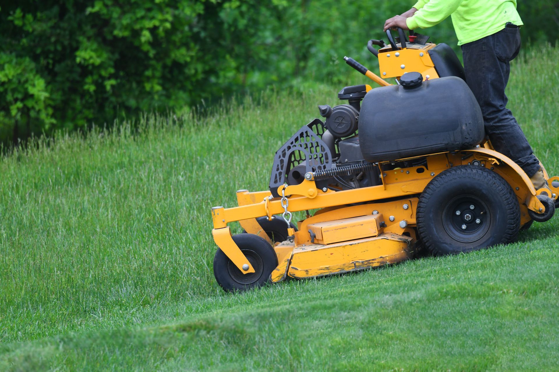 Person mowing a grassy slope with a yellow riding lawn mower Person mowing a grassy slope with a yellow riding lawn mower