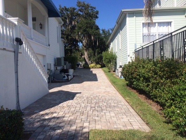 Paved driveway between white houses with stairs on the left and bushes along the right side.