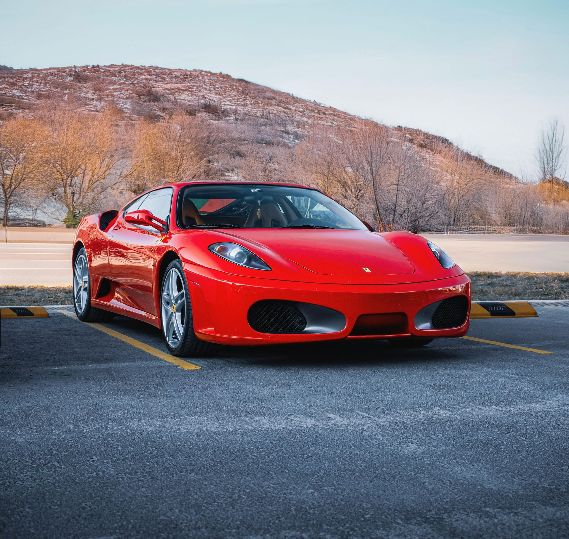 Ferrari rouge garée sur un parking, montagne en arrière-plan.