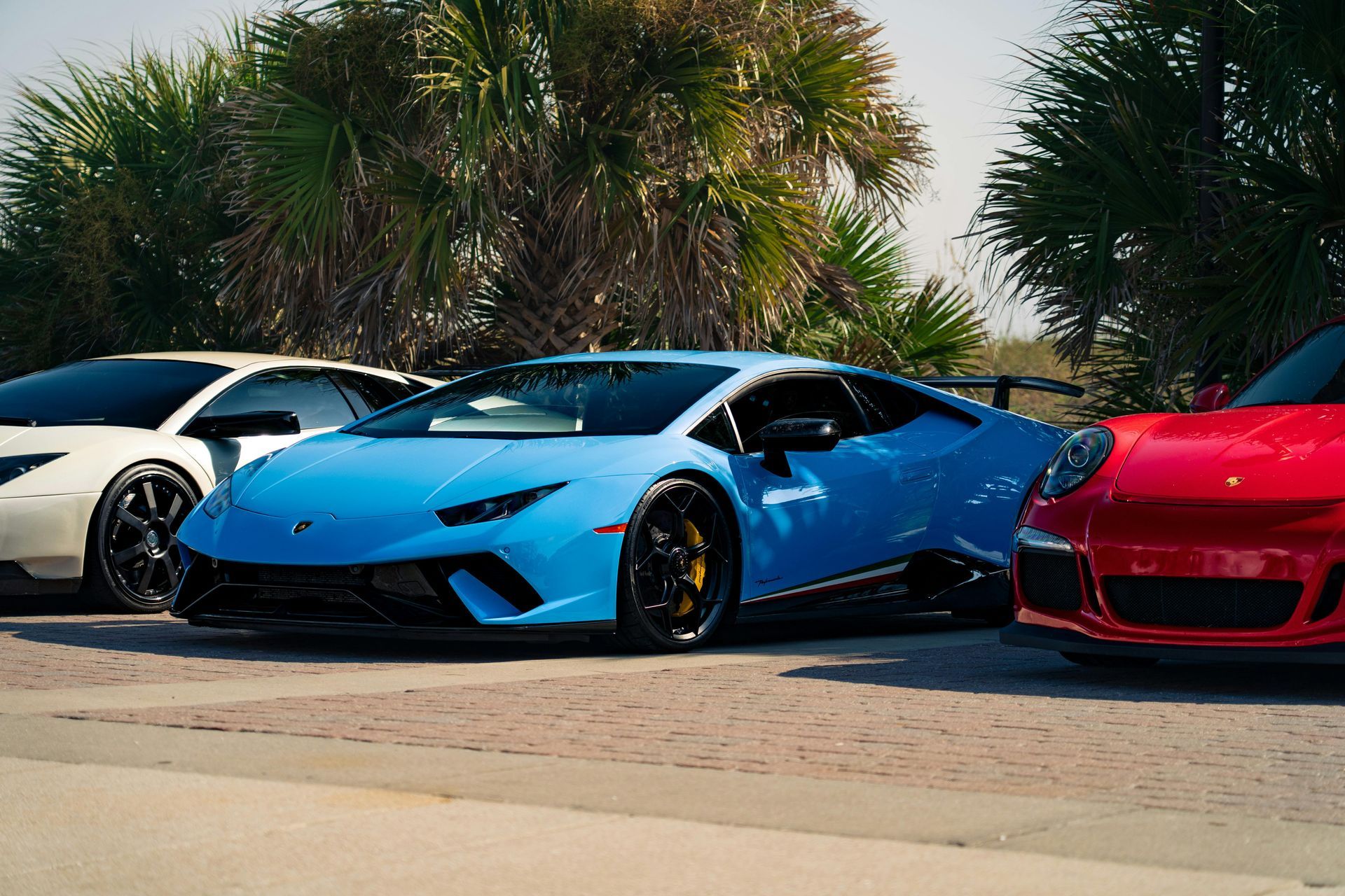 Trois voitures de sport de luxe garées à l'extérieur : une blanche, une bleue et une rouge.
