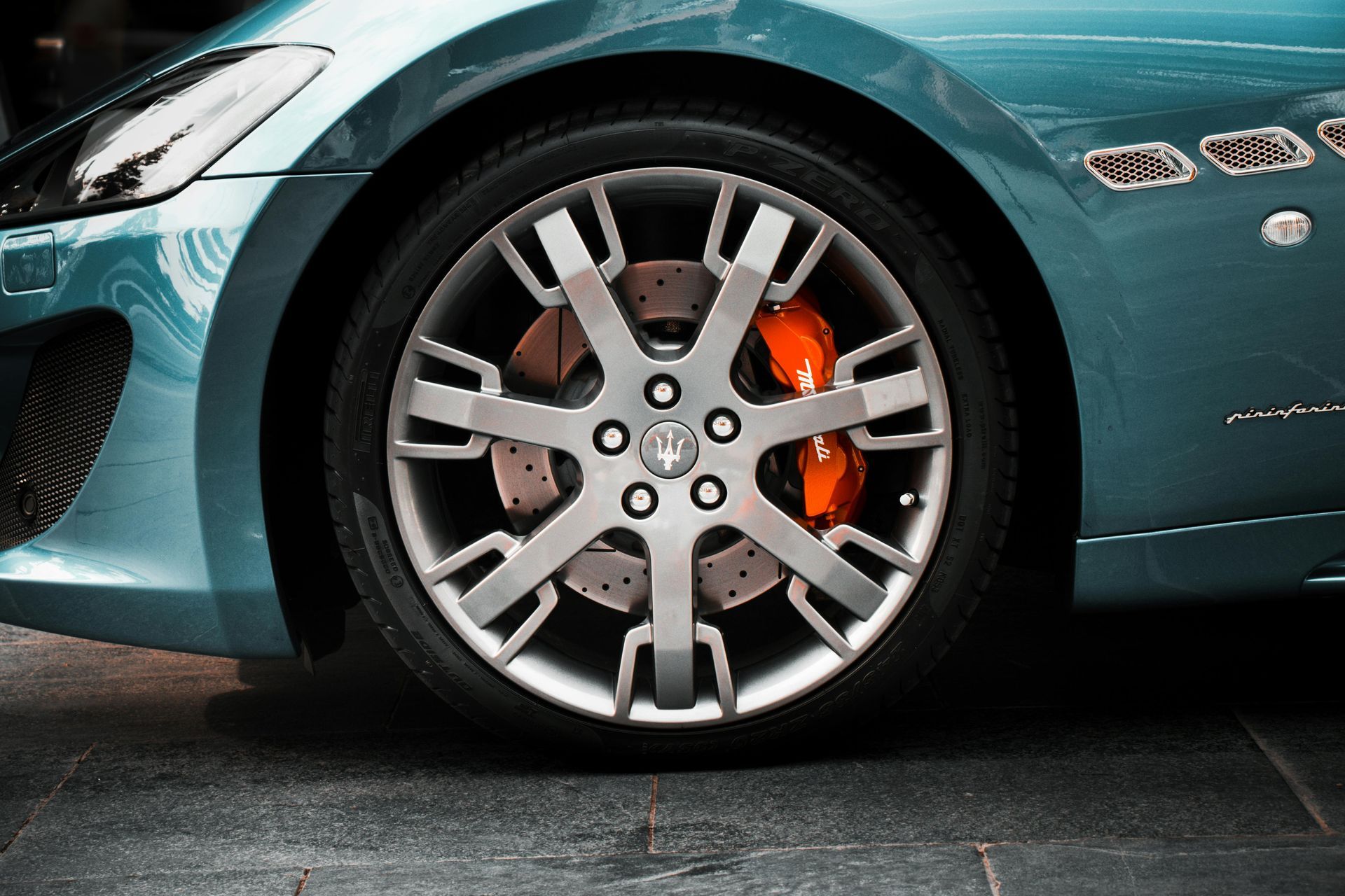 Gros plan sur une roue de voiture Maserati turquoise avec des jantes argentées et des étriers de frein orange.