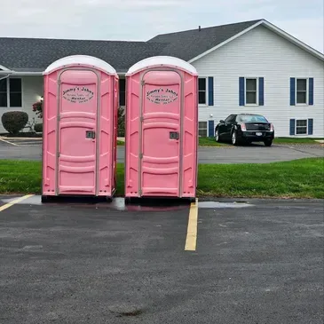 Two pink portable toilets in a parking lot in front of a house.