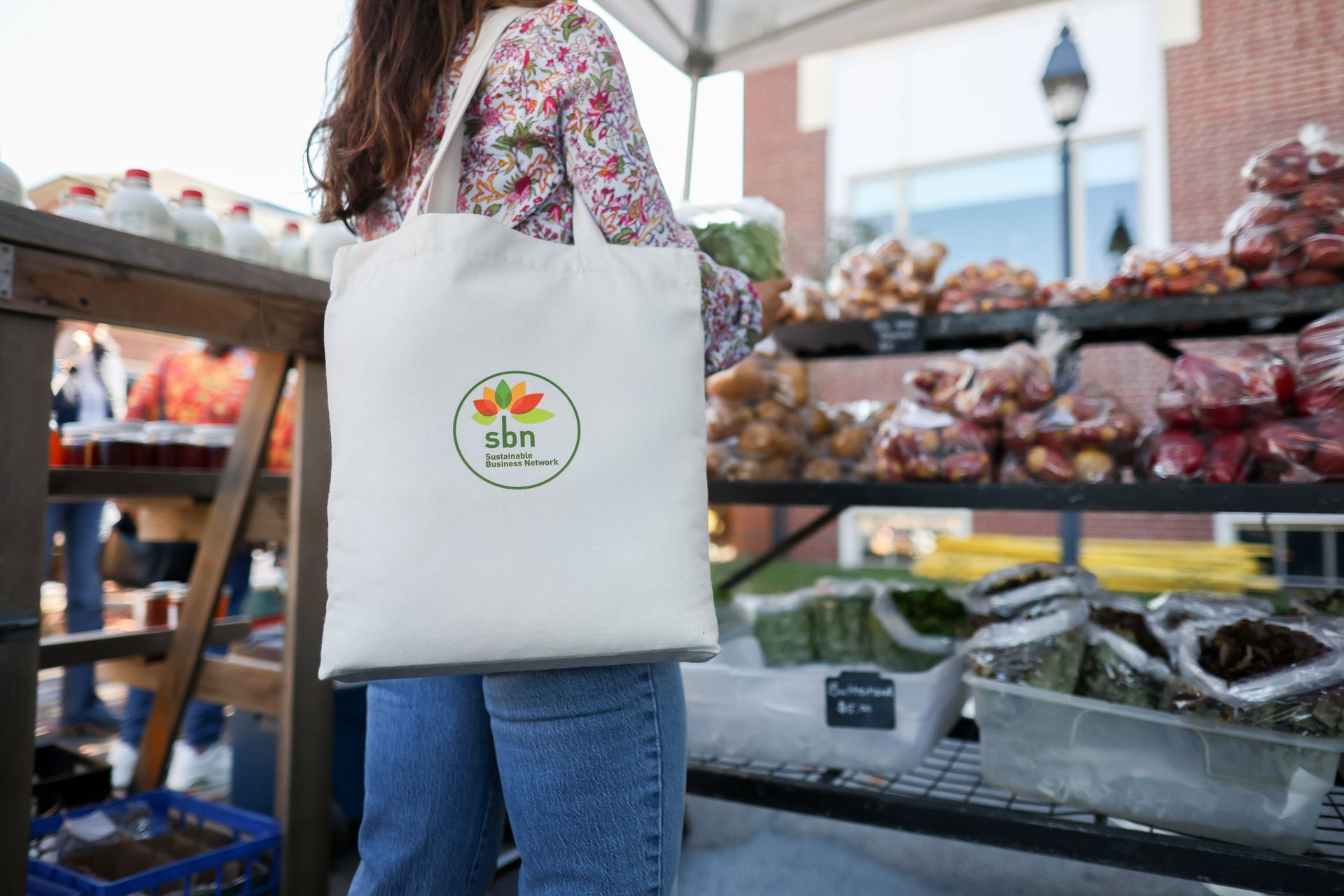 A woman is holding a tote bag at a farmers market.
