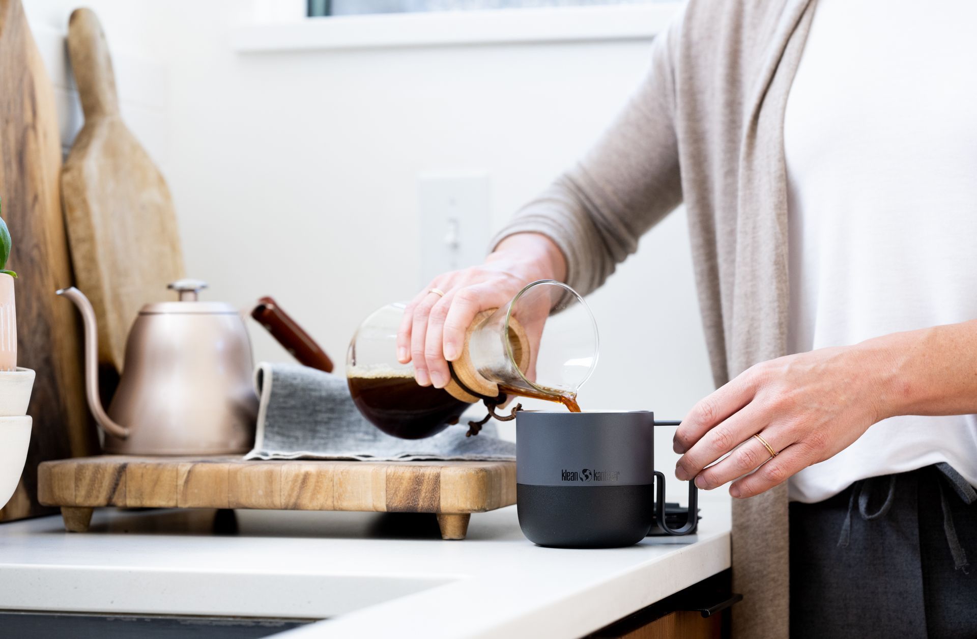 A woman is pouring coffee into a cup on a kitchen counter.