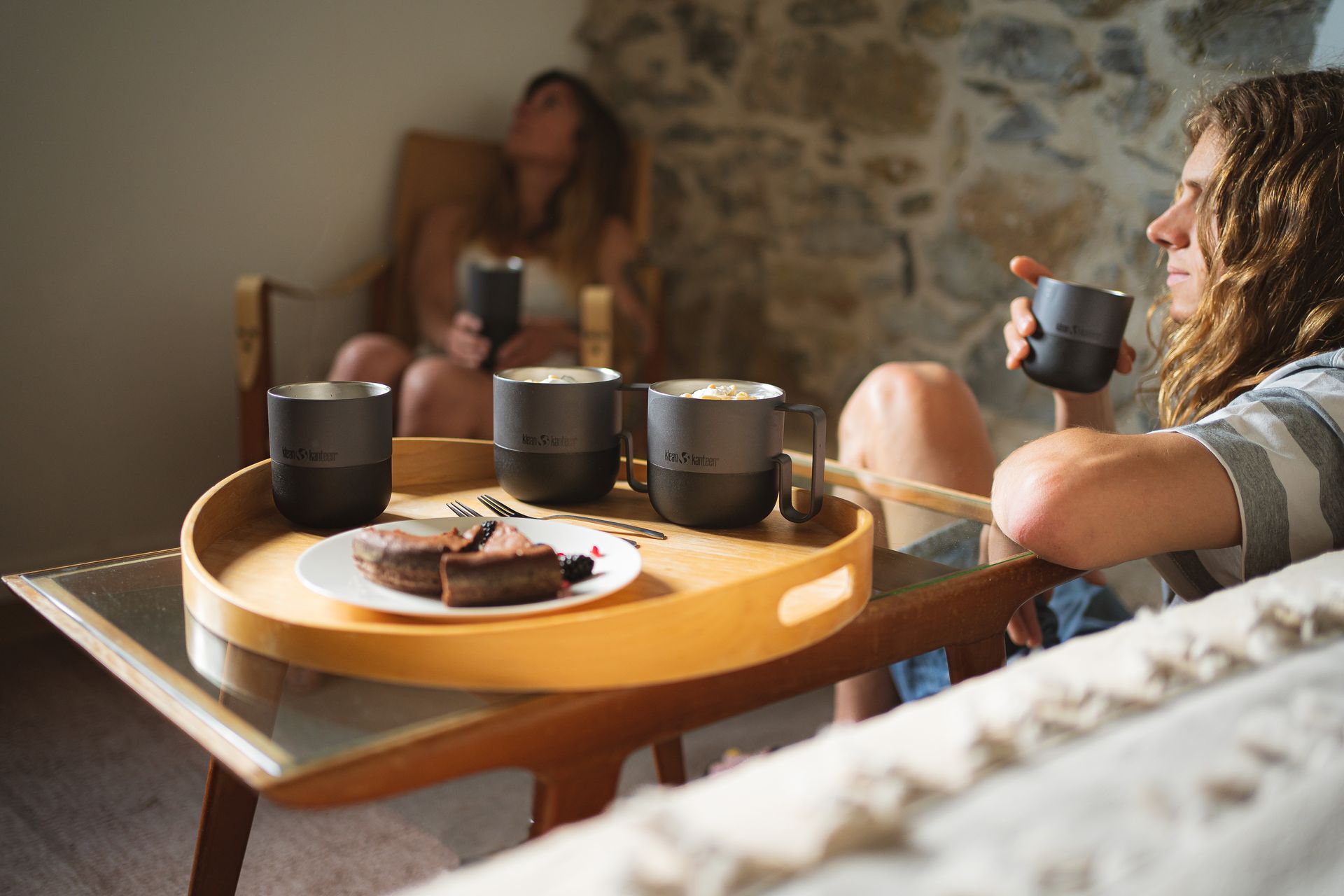 A woman is sitting on a couch holding a cup of coffee.
